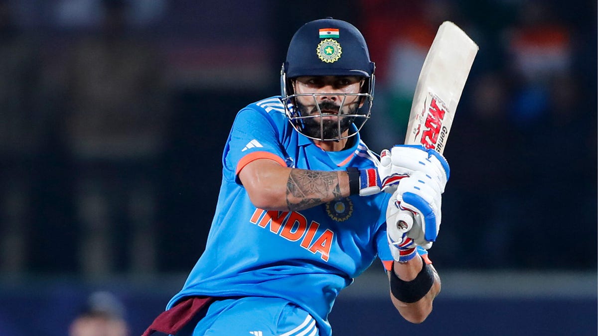 Indian cricketer Virat Kohli holds the bat with both hands, leaning back to hit the ball.