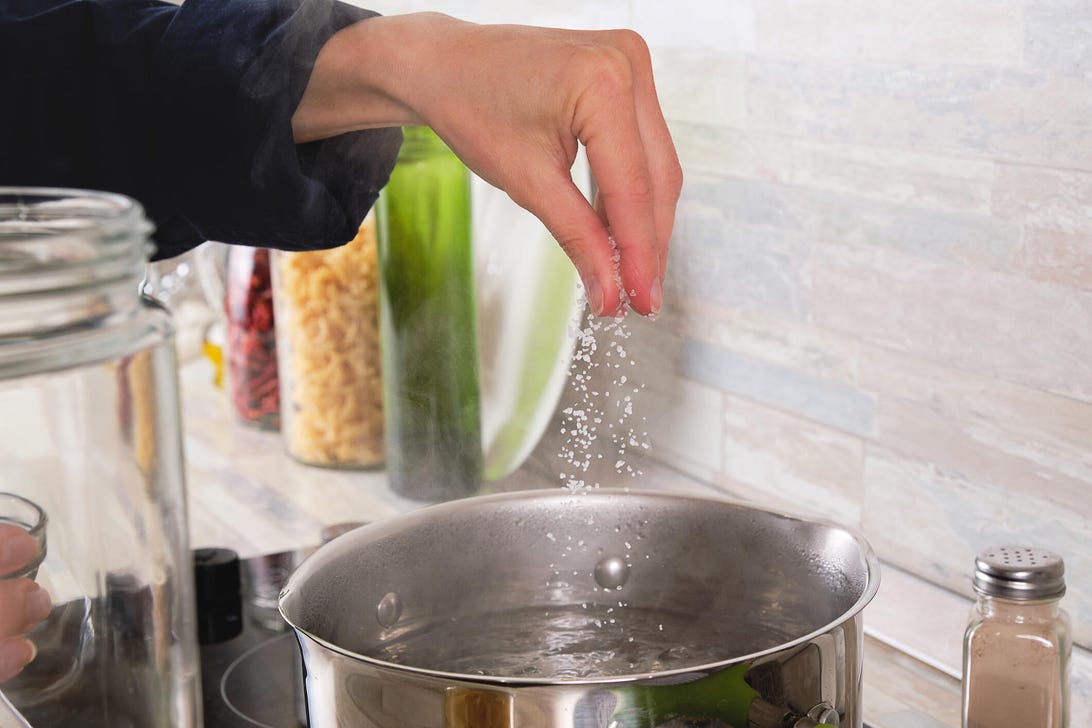 a hand sprinkles salt into a pot of boiling water