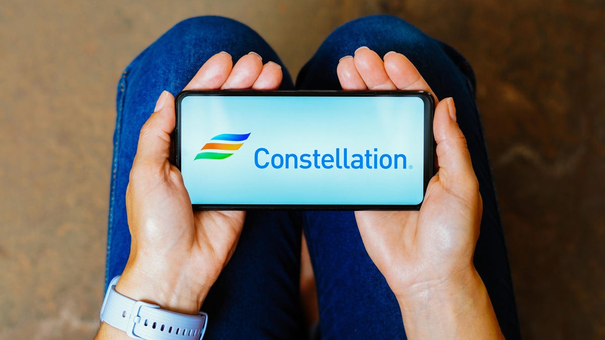 A person holding a phone with a Constellation logo showing