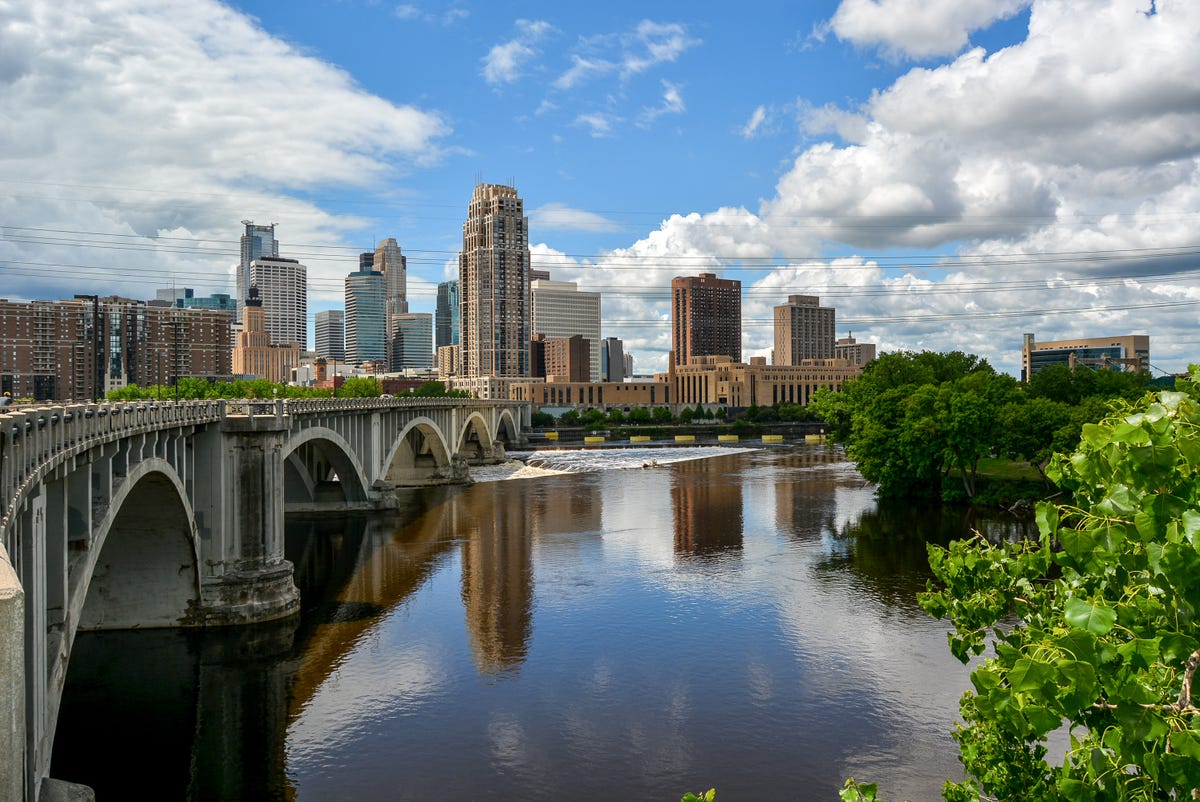 Minneapolis' Arch Bridge with the city skyline in the distance against a blue sky.
