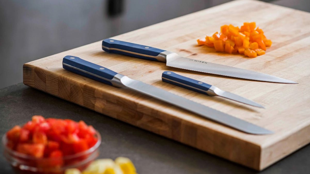 Three Misen knives rest on a cutting board next to various diced vegetables.