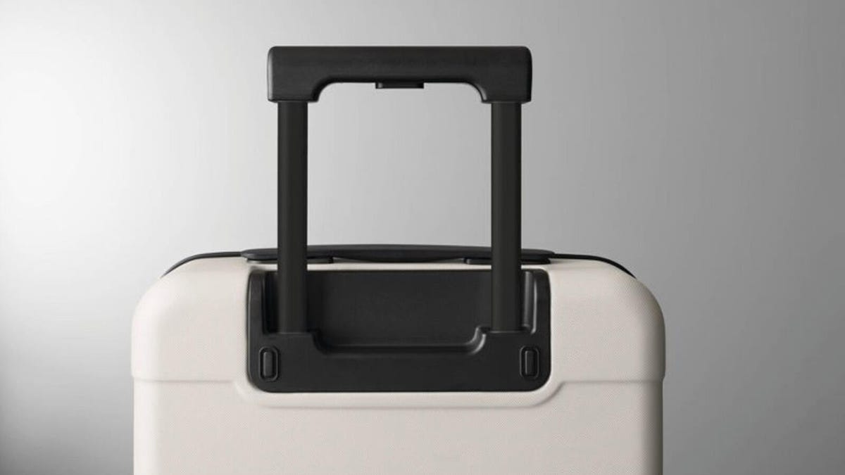 A white hardside carry-on by Made by Design with extended handle is pictured in front of a gray background.