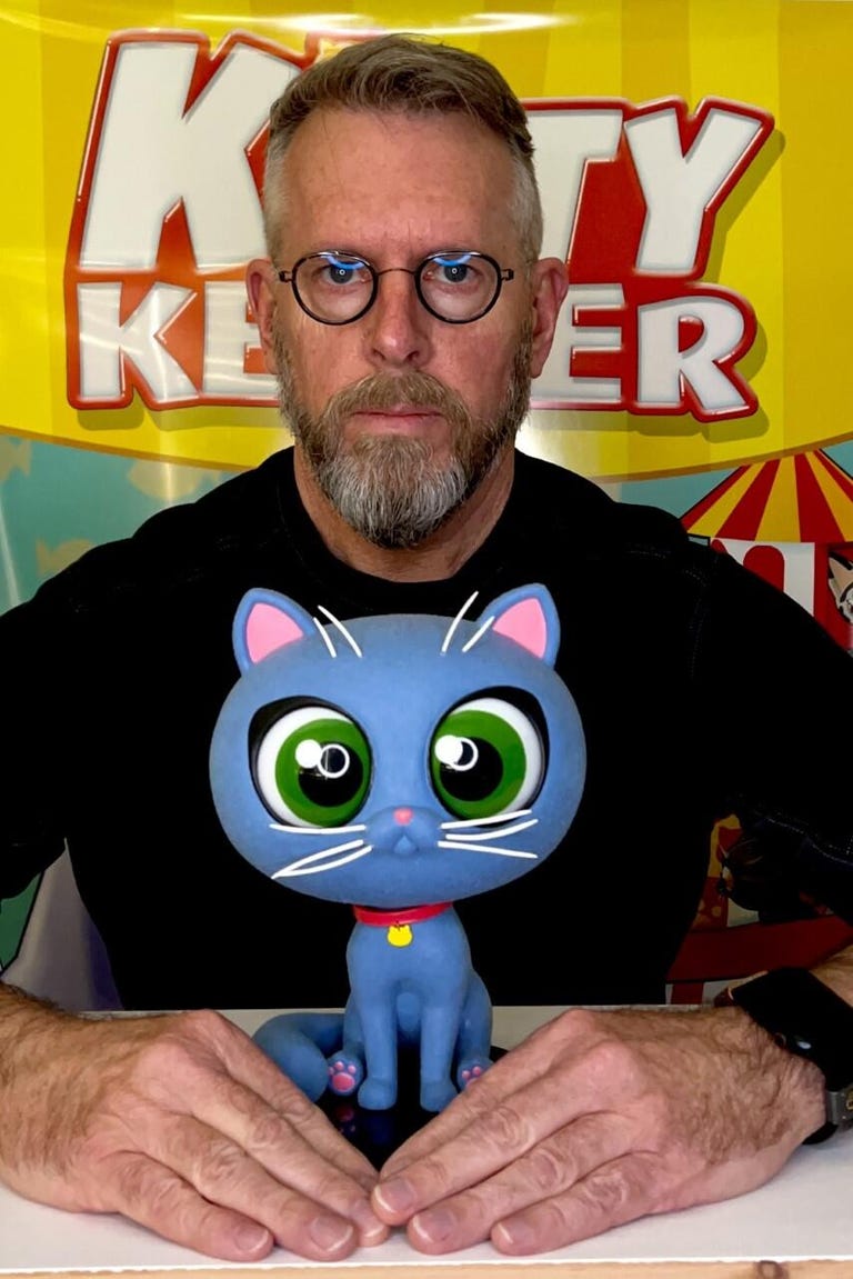 a bespectacled man with a beard and circular glasses holds a 3D printed model of a stylized, animated cat