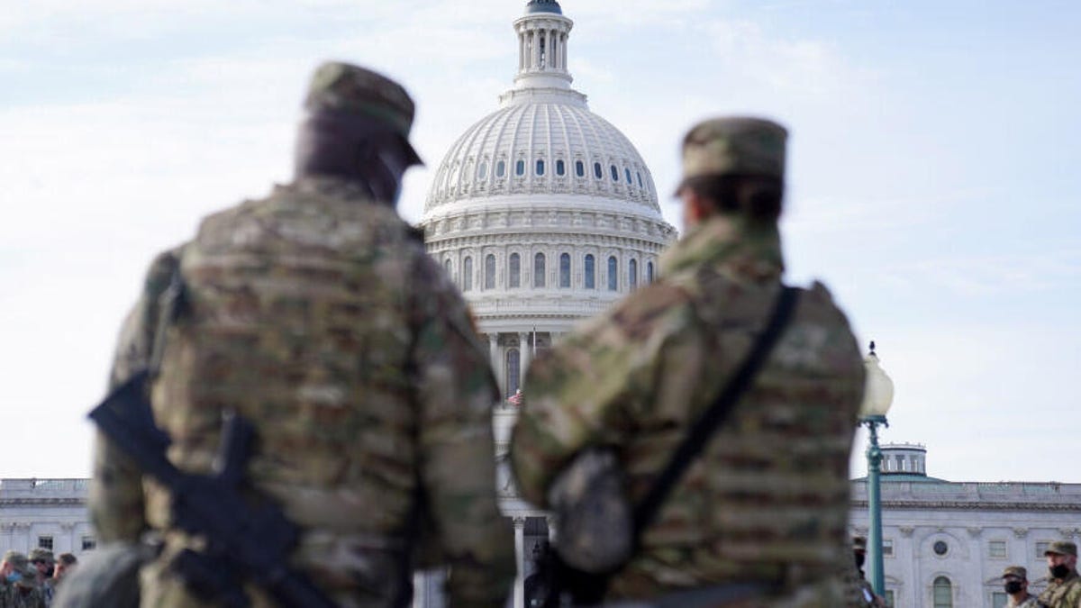 Two National Guard troops in the foreground frame a view of the Capitol dome in the distance.