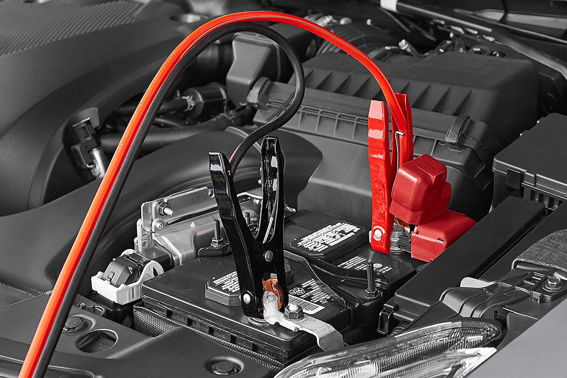 Two Amazon Basics jumper cables hooked up to a car battery
