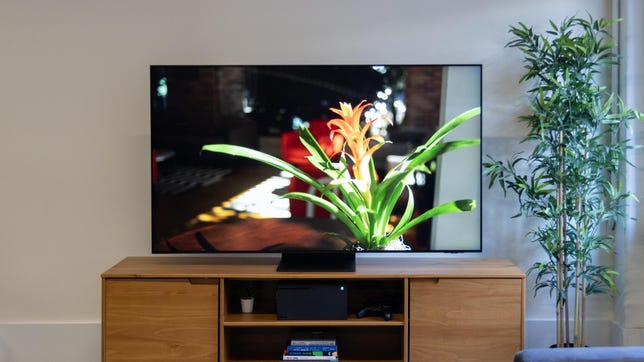 The Samsung QN90B QLED TV sits on a wooden tabletop stand.