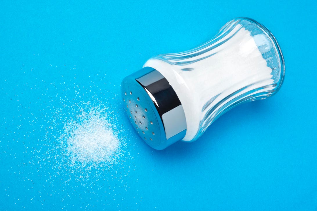 salt shaker lying on its side on a blue background with salt spilled