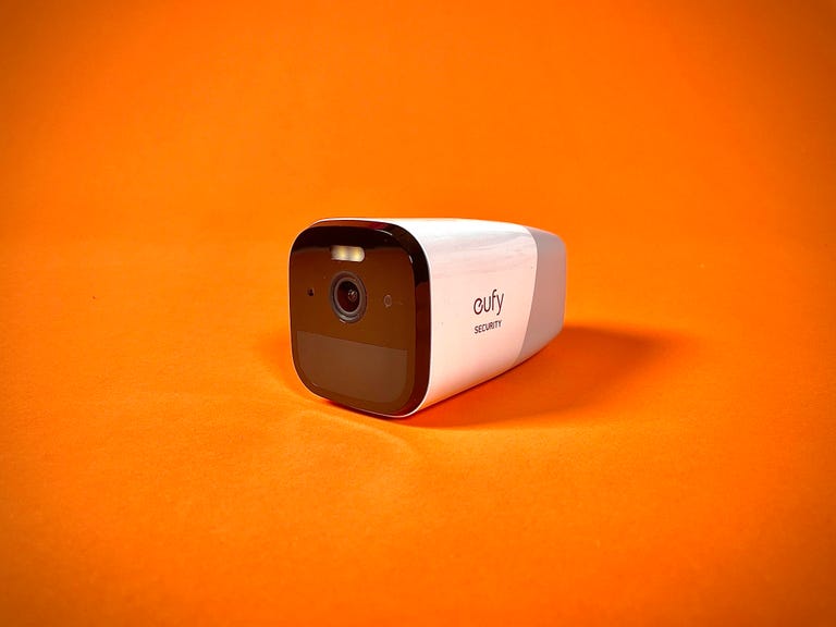 The Eufy 4G Starlight Cam against an orange background. It's a battery-powered, indoor/outdoor security camera that connects over Wi-Fi or LTE.