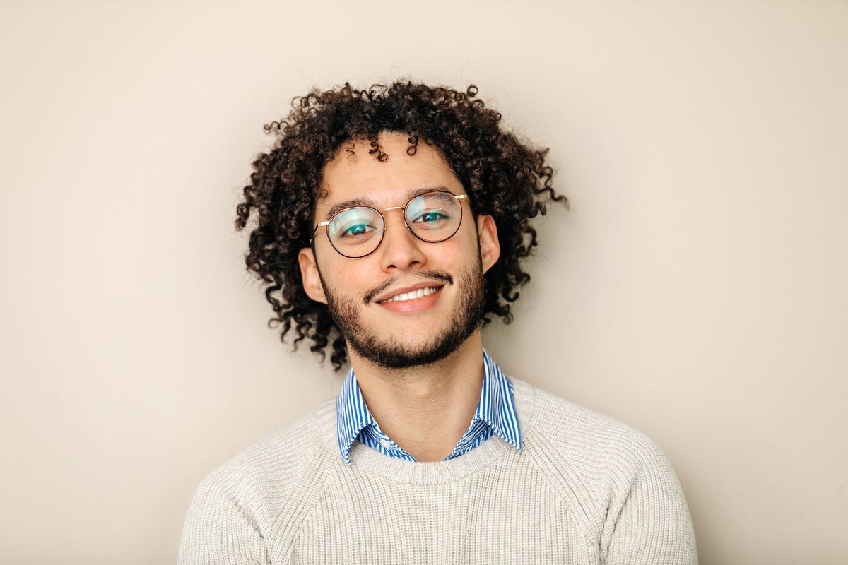Smiling man with curly hair, glasses and a sweater.