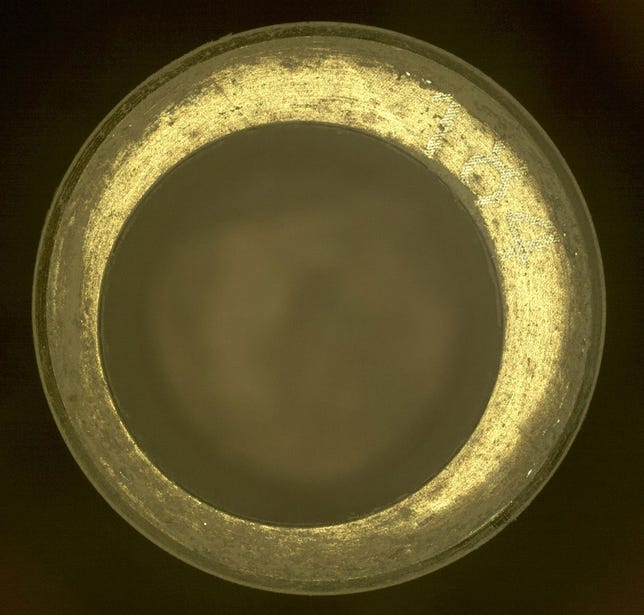 Close-up view of the circular opening of a gold-colored sample tube.