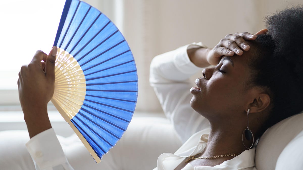 A reclining woman fans herself with one hand on her forehead