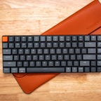 The Keychron K3 mechanical keyboard with its orange case against a wooden background.