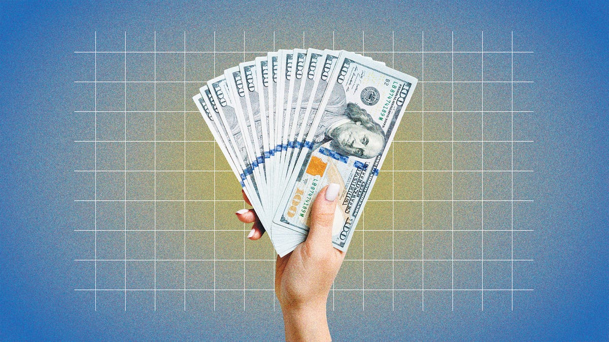 a hand holding a fan of $100 bills against a blue grid background