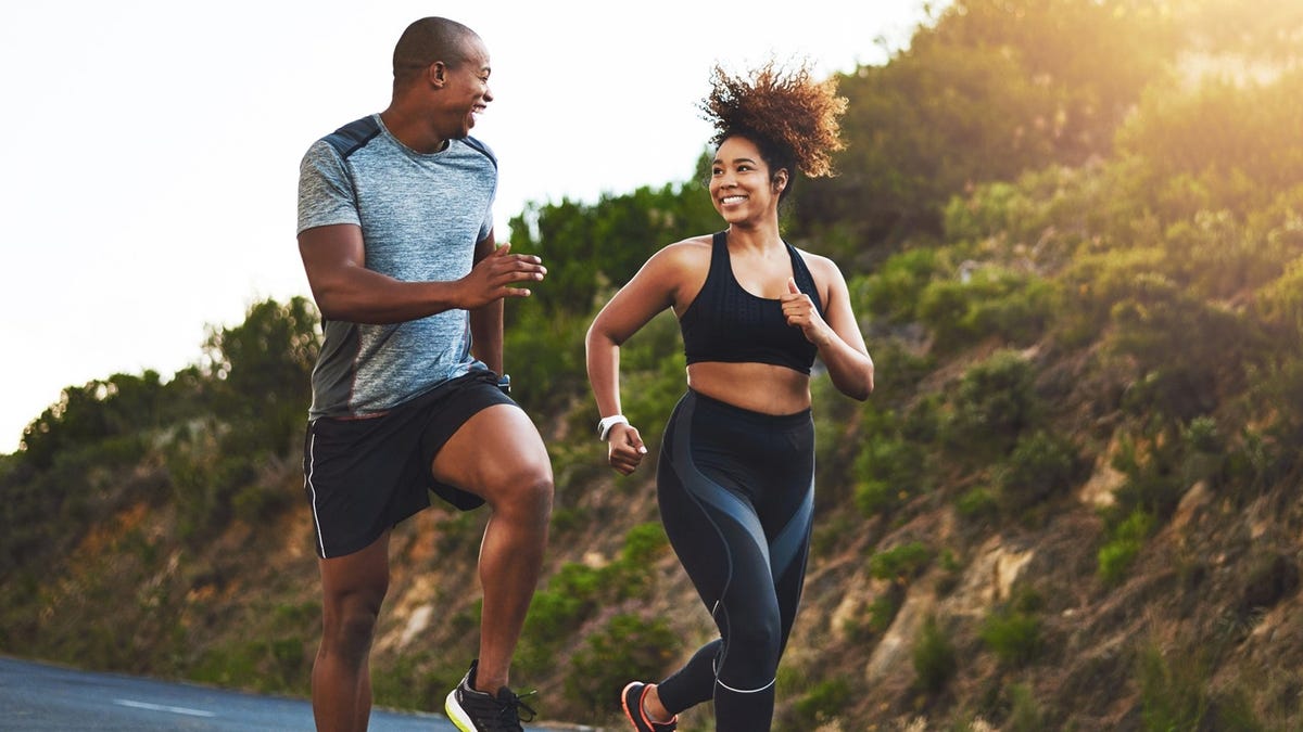 A man and woman smile at each other while running in the sun