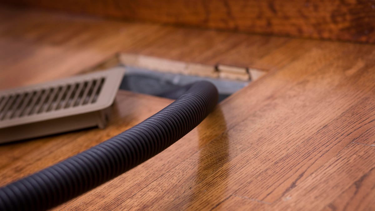 a vacuum cleans out an air vent in a hardwood floor