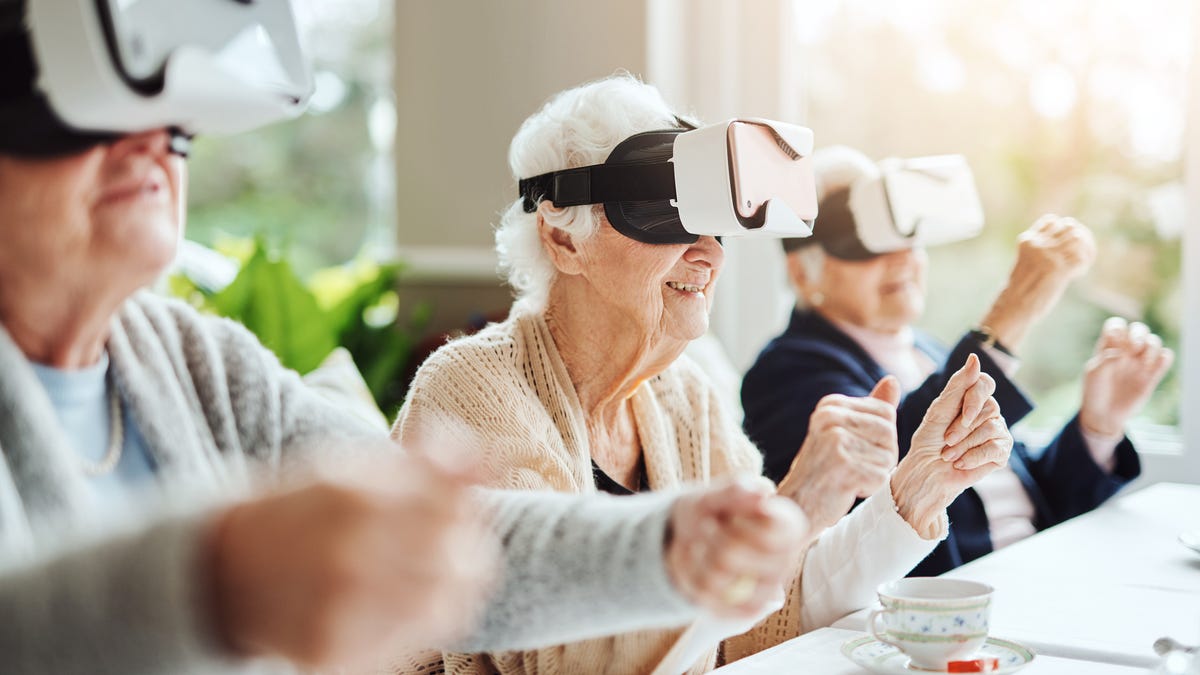 Three senior citizens seated at a table wearing VR headsets, playing a game