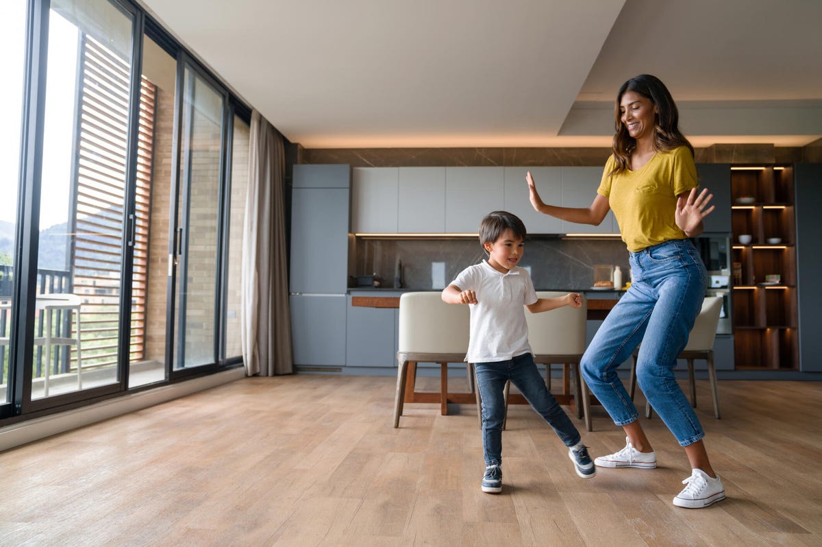 Mujer joven baila con un niño pequeño en casa espaciosa.