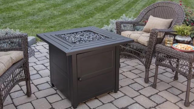 Outdoor propane fire pit sitting on brick pavers with wicker chairs around it