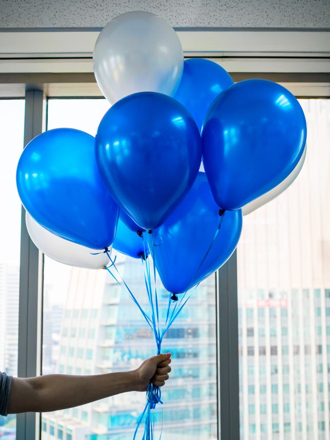 A hand holding up a cluster of blue and white balloons in an office.