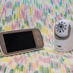 A baby monitor and screen sitting on a pastel blanket 