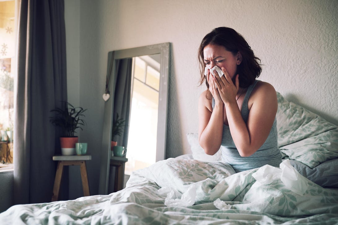 A woman sneezing into a tissue in bed