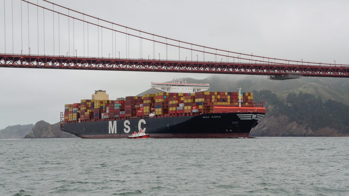 A container ship laden with multicolored containers passes under San Francisco's Golden Gate bridge, which is nearly covered in fog.