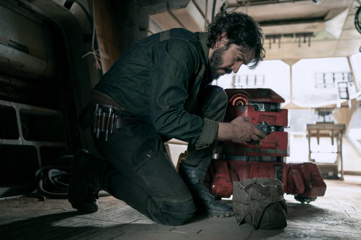 Cassian Andor crouches next to the cute red B2EMO droid in Andor.