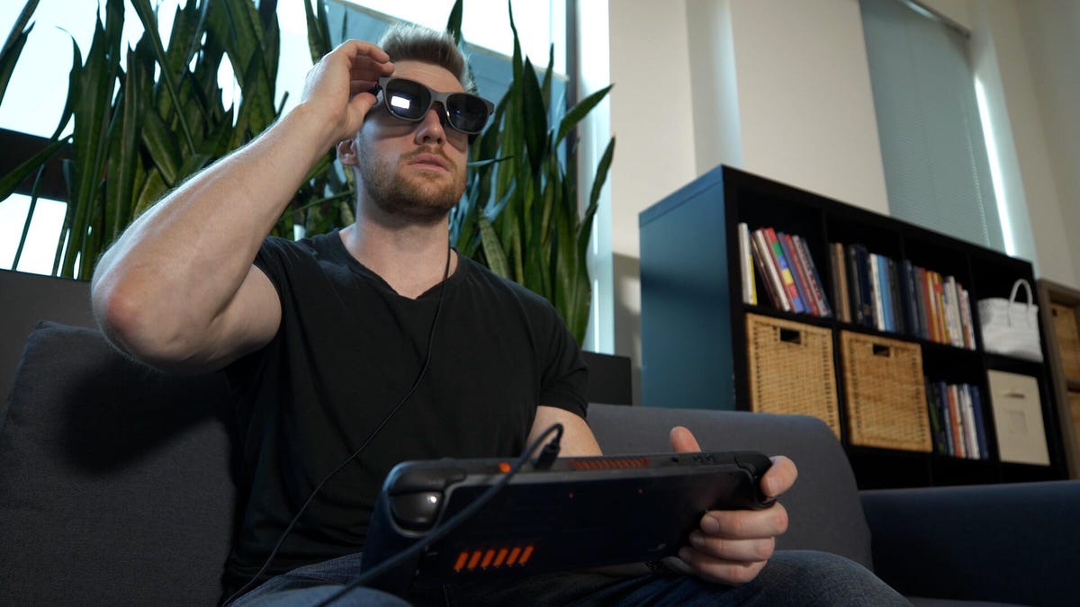 ο άνθρωπος ρυθμίζει τα γυαλιά Xreal και κρατά ένα Steam Deck