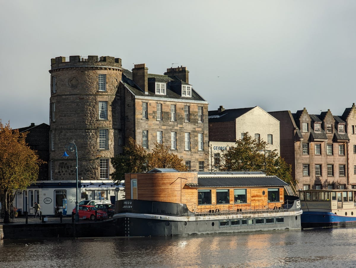 An image showing a boat on a river with buildings behind.