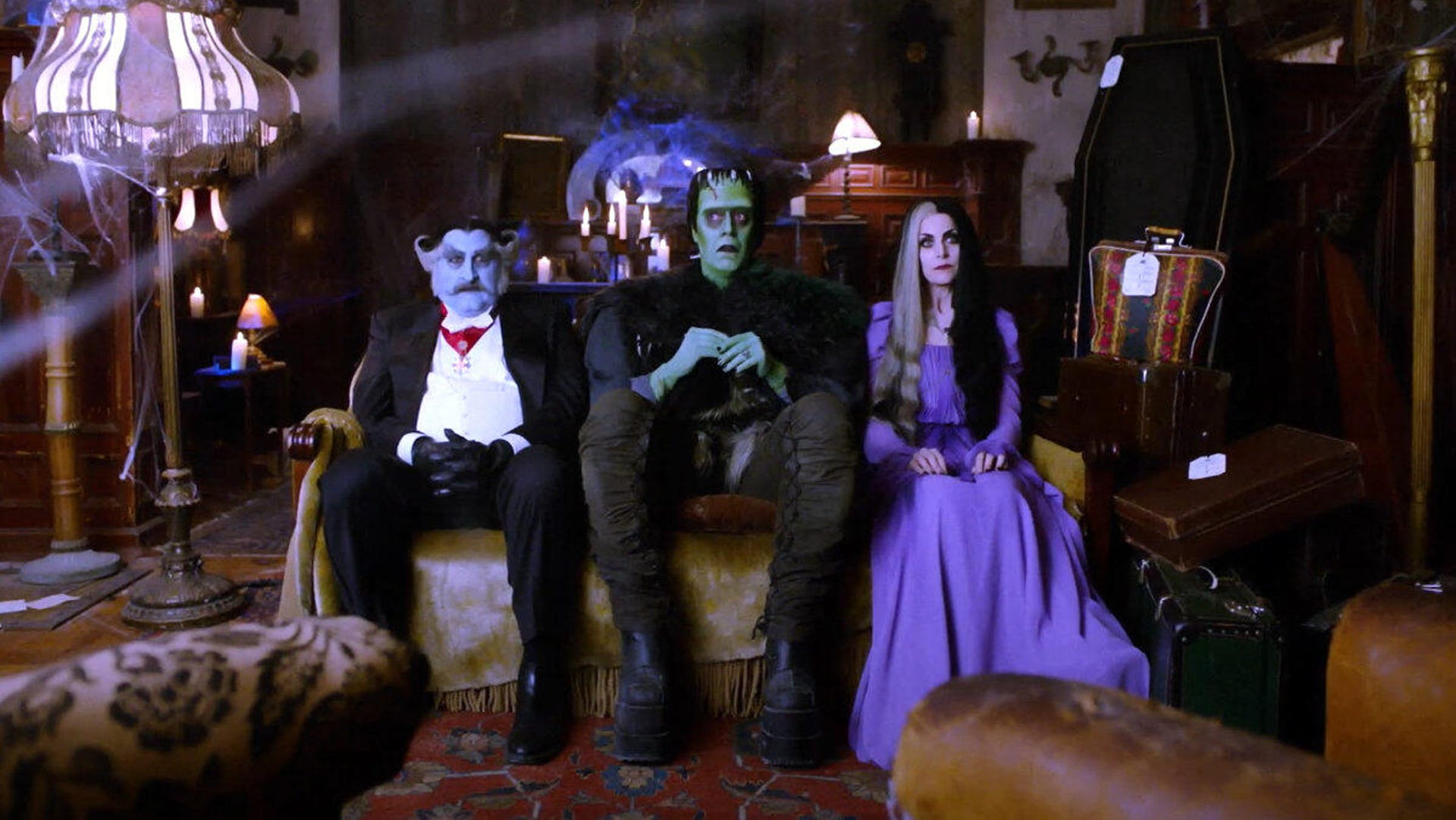 Grandpa, Herman Munster and Lily Munster sit on a couch together in color in a teaser screenshot from Rob Zombie's The Munsters.