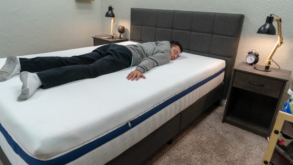 A man sleeping on his stomach on a mattress in a bedroom