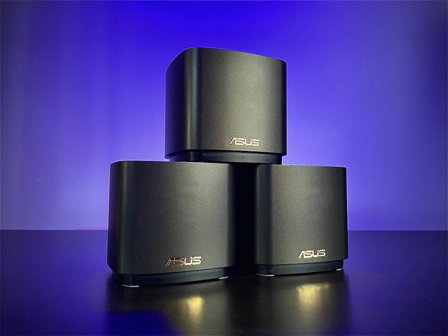 Three Asus ZenWifi AX Mini mesh router devices sit in a pyramid against an indigo background.