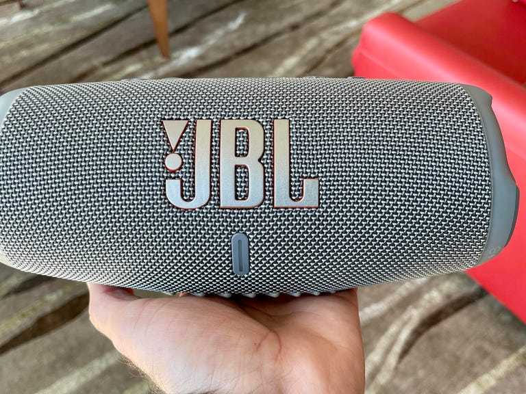 The JBL Charge 5 in gray is being held in the palm of a hand.