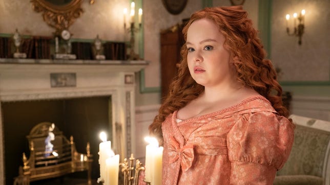 Penelope from Bridgerton sits in a Regency-period gown inside an opulent room lit by candles.