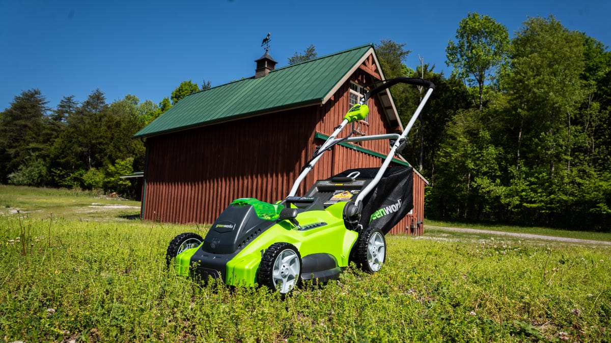 A green Greenworks mower in a field with a building behind it.