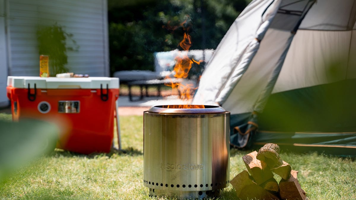 A Solo Stove fire pit is burning logs outside of a tent.