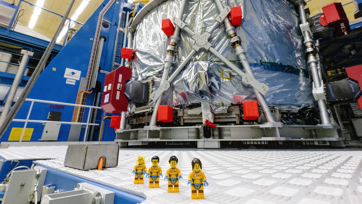 Four Lego figures dressed in yellow stand in front of Artemis moon mission equipment.