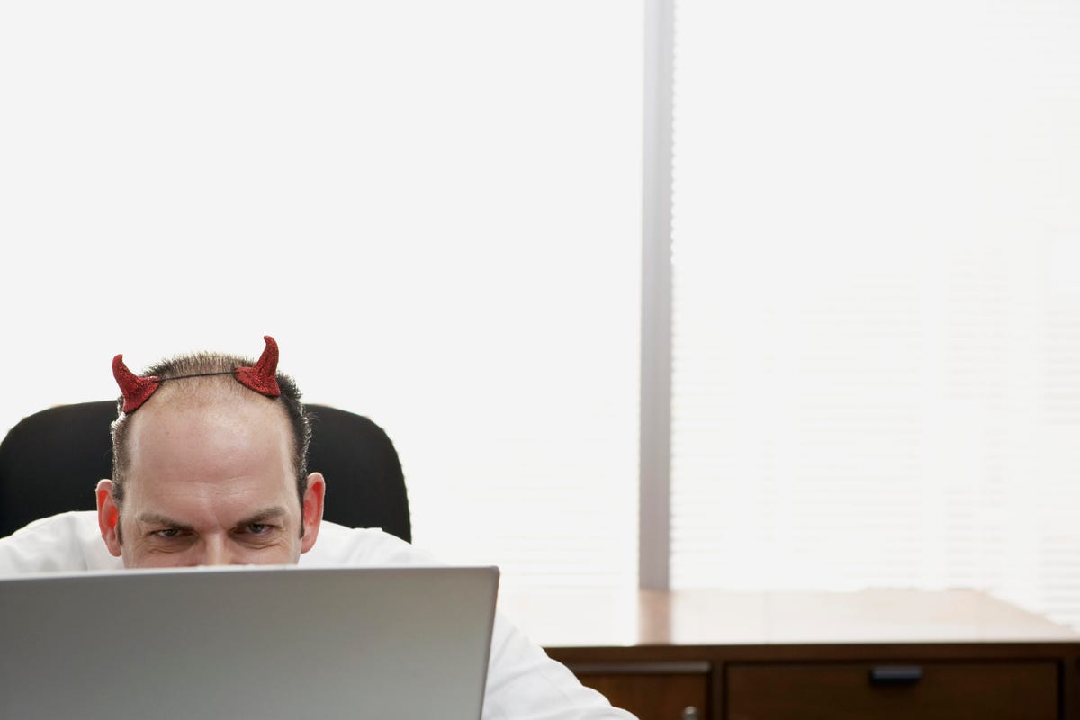 Mature businessman with devil horns using laptop in office
