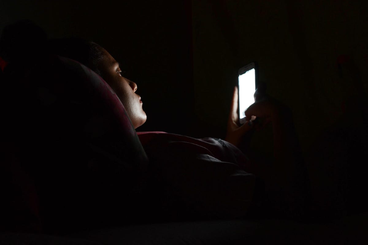 Side View Of Woman Using Phone While Lying In Darkroom