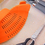 An orange strainer in a drawer of kitchen tools