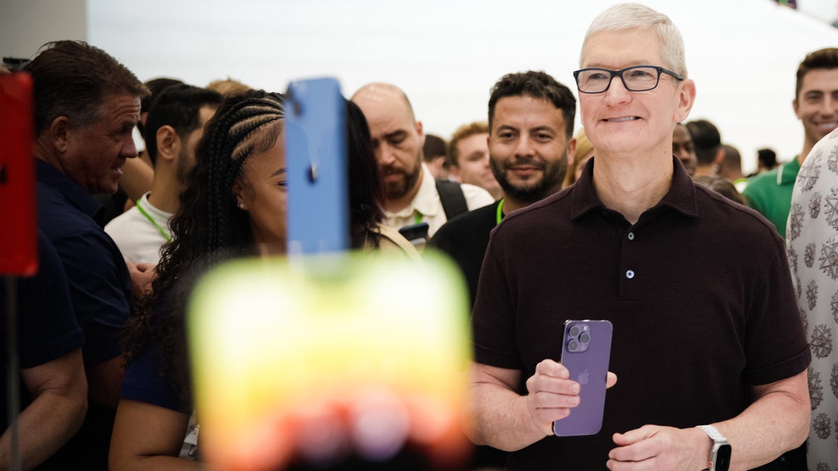 Tim Cook smiling and holding an iPhone 14 in front of a crowd of people