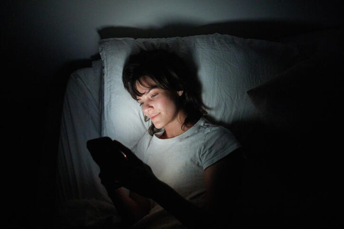 Young woman using her cellphone while lying in bed at night.