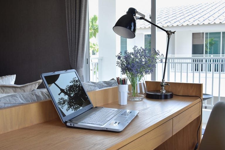 wooden table with computer notebook,pencil,lamp and artificial flowers in modern working area