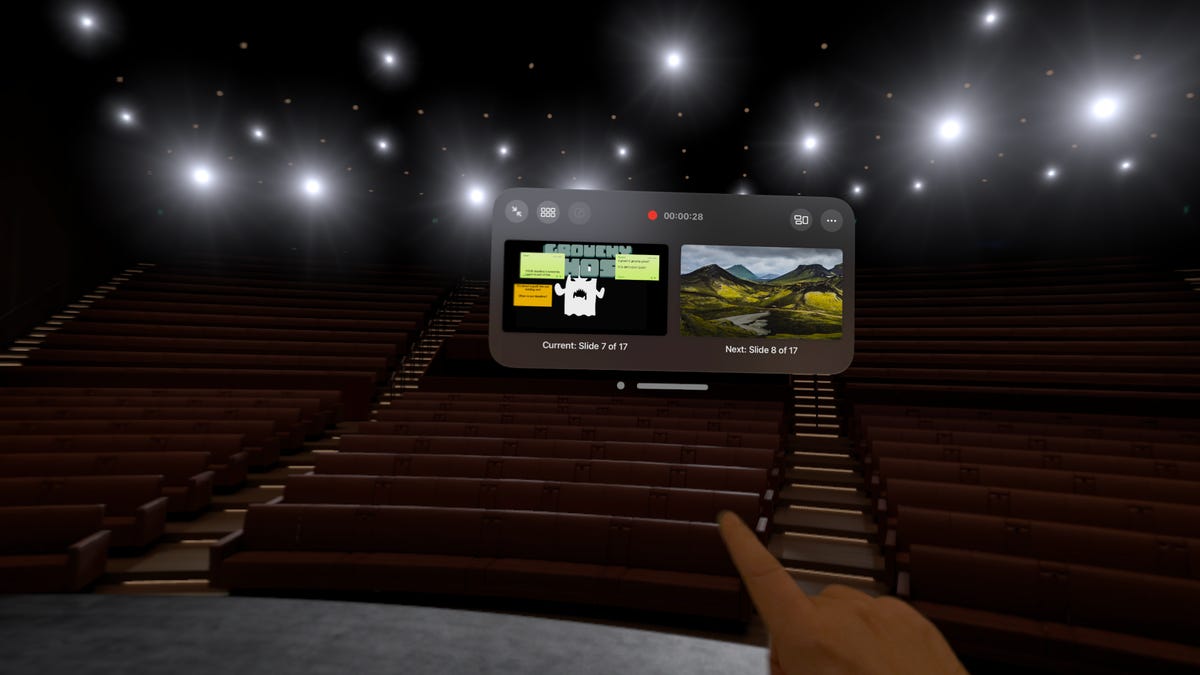 A virtual Steve Jobs Theater in Apple Vision Pro with a real hand pointing at a slide deck