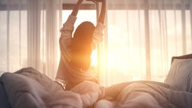 Woman stretching in bed after waking up to the morning sun.
