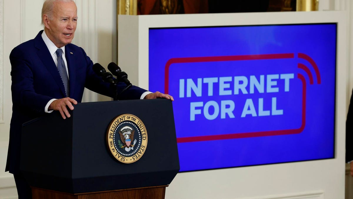President Biden stands at a podium with the official seal, while behind him a screen says 'Internet For All'