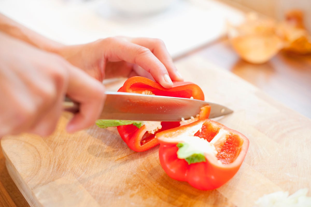 Red bed pepper on a cutting board with hands and knife slicing it