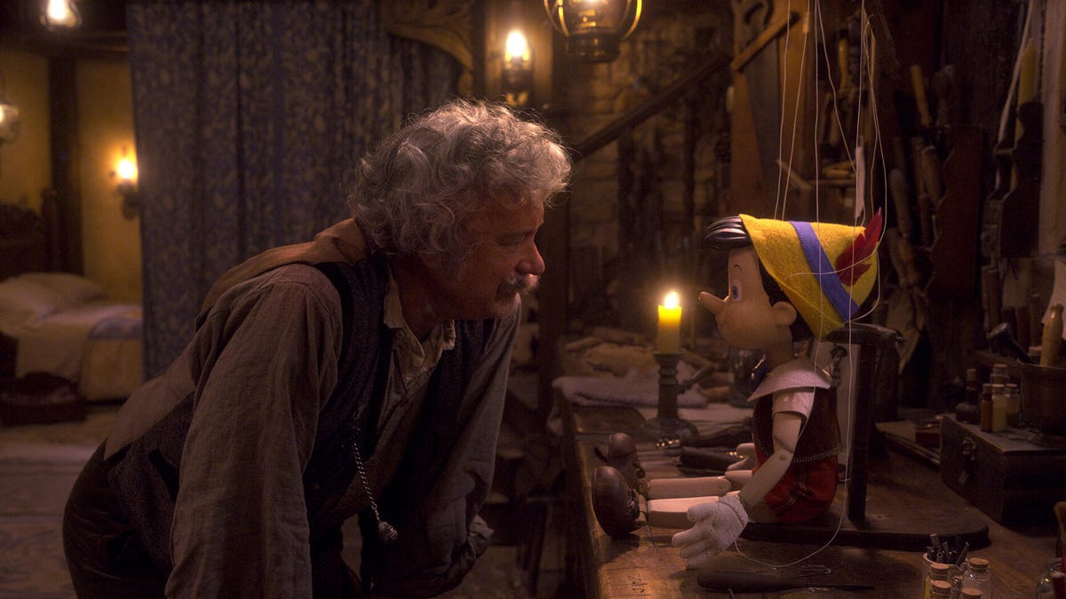 Tom Hanks as toymaker Geppetto with a mighty gray mustache, leaning down to study a puppet in Disney&apos;s live-action Pinocchio.
