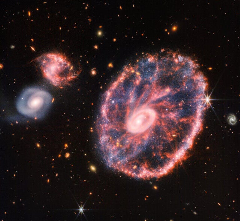 A round, reddish galaxy with a circular center glows against a dark starry background.