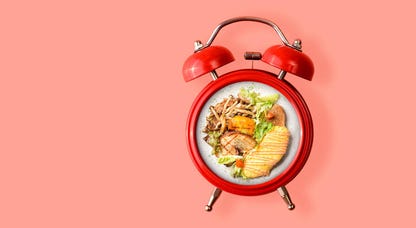 Food in an alarm clock over a pink background.
